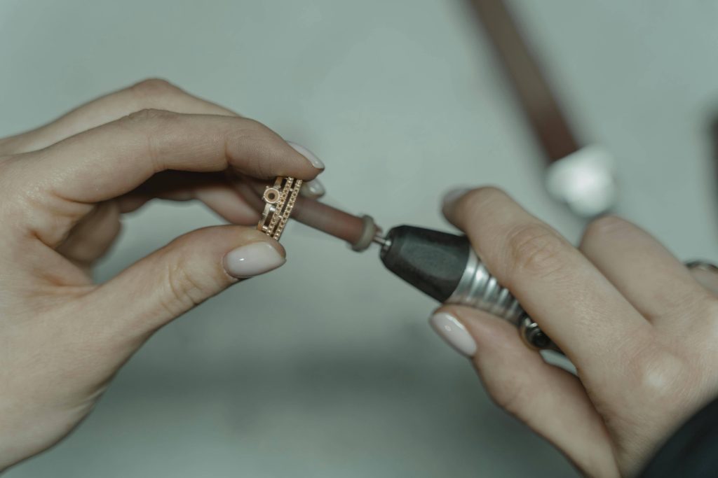 une paire de mains manucurés d'une femme tiennent un outil qui sert à polir des bijoux. la femme polit avec cet accessoire une bague en or